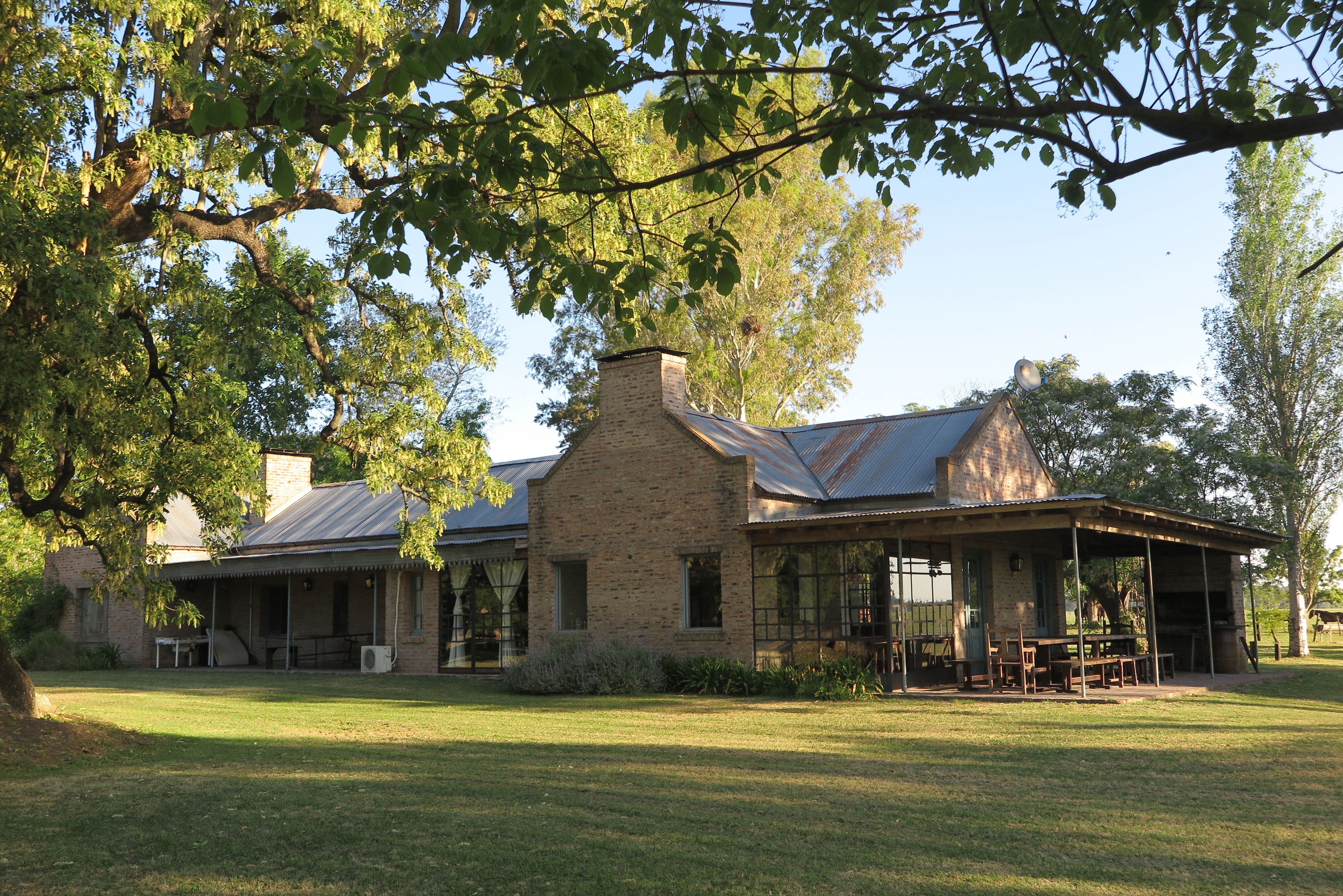 La casa de campo con la galería y la mesa larga bajo el alero.